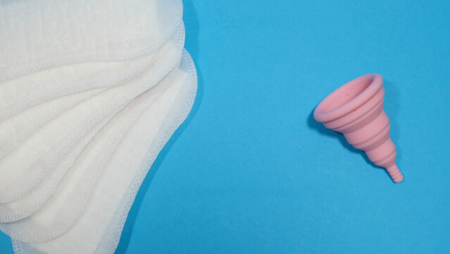 Copa menstrual rosa plegable y compresas desechables en un fondo azul. Transici&oacute;n a la menstruaci&oacute;n sostenible