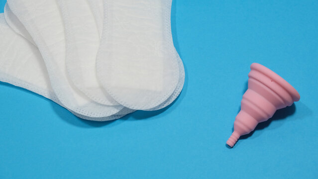 Copa menstrual rosa plegable y compresas desechables en un fondo azul. Transici&oacute;n a la menstruaci&oacute;n sostenible