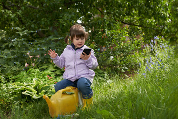 A little girl promised to water a flower bed, but sat down on a bucket and communicates or watches...
