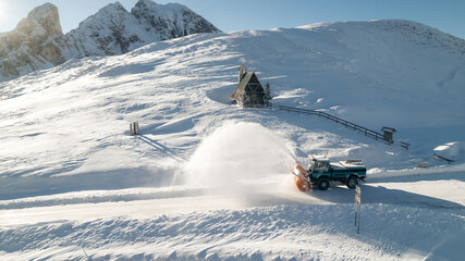 Snow Plow Truck cleaning the road in the mountains. Italy. A tiny wooden mountain hut and mountain...