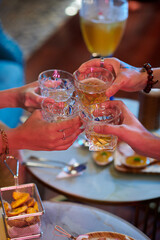 Hands of friends clinking glasses over table with snacks at party