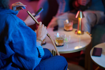 Young woman using personal mouthpiece when smooking hookah with friends - obrazy, fototapety, plakaty