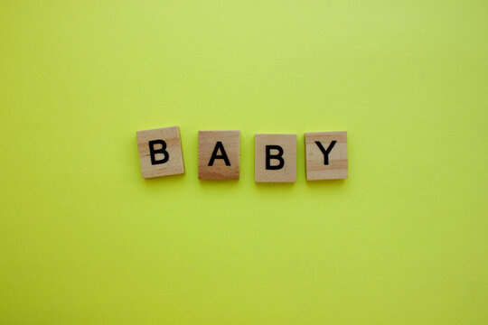 The word BABY is made of wooden cubes on a yellow background.