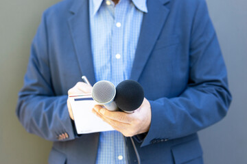 Journalist at media event or news conference, holding microphone, writing notes. Broadcast...