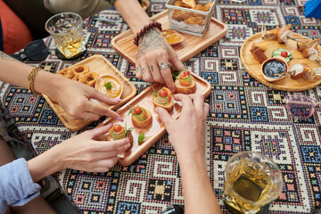Hands of young people taking snacks from wooden plate on cafe table