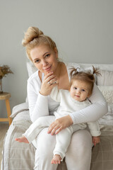 Portrait of young tired Mother and baby girl looking at camera in bedroom home. Child care, domestic life routine, healthy lifestyle. Exhausted woman take care about child and vertical