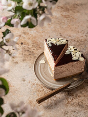 Two pieces of chocolate cheesecake with almond petals in ceramic rustic plate on brown textured background. Spring flowers in blur. Seasonal menu