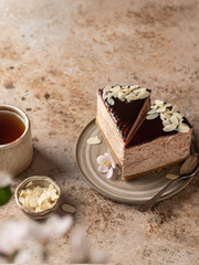 Two pieces of chocolate cheesecake with almond petals in ceramic rustic plate on brown textured background. Spring flowers in blur. Text space, menu