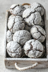 Chocolate chip cracked cookies close up. Wooden rustic box with fresh baked chocolate crinkle cookies in icing sugar on gray textured background