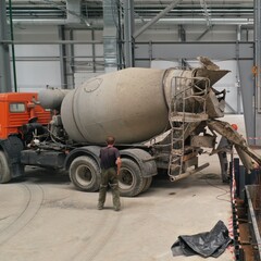 Fototapeta na wymiar Pouring concrete mortar from a concrete mixer inside a huge production hangar. Filling the construction pit with cement mortar. Gray concrete mixer with orange cab.