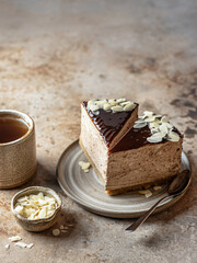 Two slices of chocolate cheesecake with almond petals, tea cup on brown textured background. Text space, menu