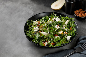 Diet salad with green arugula, feta cheese and pears, almond nuts. Delicacy fresh Green fruit salad on dark background.