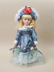 Vintage porcelain doll baby girl with blue eyes, blonde curls, wearing a blue hat decorated with red flowers and a blue satin dress. - 556173295