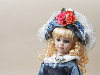 Vintage porcelain doll baby girl with blue eyes, blonde curls, wearing a blue hat decorated with red flowers and a blue satin dress. - 556173296