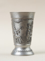 Traditional German vintage  pewter wine glass with a bas-relief depicting a man sitting under a tree holding out a purse to a woman - 556173613