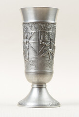 Traditional German vintage  pewter wine glass with a bas-relief depicting a man sitting under a tree holding out a purse to a woman - 556174031