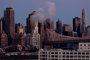 Queensboro Bridge city skyline at dawn with steam from smoke stack.