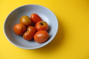 homemade tomatoes of different colors red yellow orange lie in a gray plate on a yellow background with a place for text copyspace. Side view from above