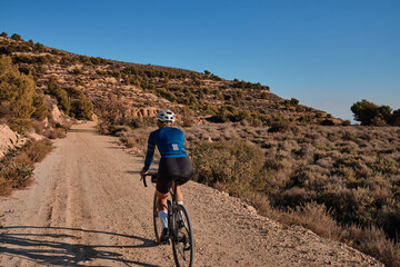 woman cyclist riding a gravel bicycle on the road in hills with mountain view, Alicante region in Spain 