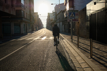 Naklejka na ściany i meble Man rides a bicycle in an empty city at sunset Empty city road with cycling man silhouette at summer sunset.