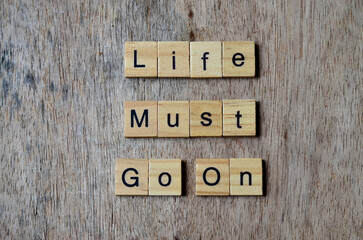 life must go on text on wooden square, inspiration quotes