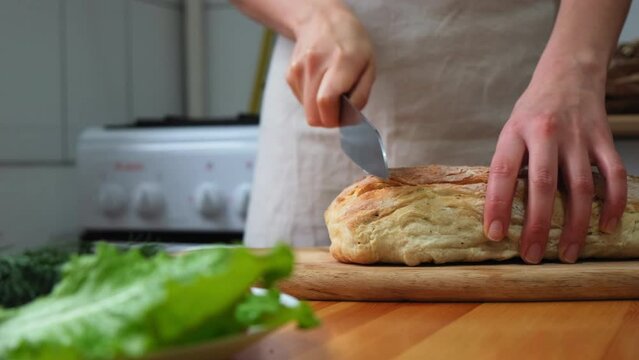 cook slices ciabatta. food cooking, baking and people concept - female baker with knife cutting loaf of bread to slices at bakery or kitchen. Cooking the ciabatta. Italian bread. Baking bread.