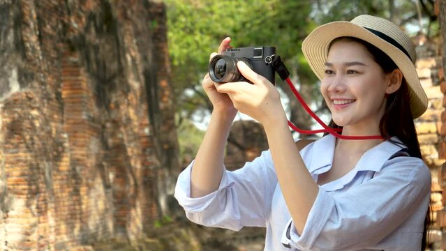4K portrait, beautiful young Asian tourist girl in hat take a photo in the archaeological site at Ayutthaya, Thailand. Traveling, historical