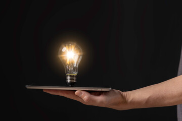 Businessman holding a bright light bulb on tablet. Concept of Ideas for presenting new ideas Great...