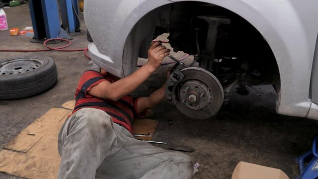 Expert Latino Mechanic Lying on the Floor Fixes Car Brake Pads with Hand Tools. Using his bare hands to change a customer's brake disc brake pads at a Mexican auto shop in Cancun 4K Slowmotion