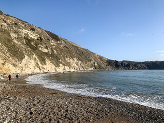 Lulworth Cove, Dorset, England, UK. Public beach view in Lulworth Cove. Lulworth Cove and beach view. Winter sunny day morning. People are walking along the sea