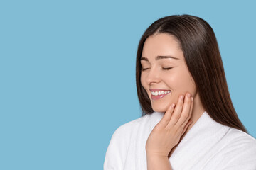 Portrait of attractive young woman in bathrobe on light blue background, space for text. Spa treatment