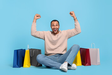 Happy African American man with shopping bags on light blue background