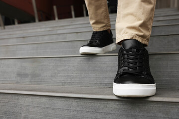 Man in stylish black leather sneakers walking down stairs, closeup. Space for text
