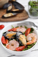 Bowl of delicious salad with seafood on white wooden table, closeup