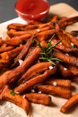 Delicious sweet potato fries and sauce on parchment paper, closeup