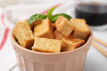 Delicious fried tofu with basil and sesame seeds in bowl on table, closeup