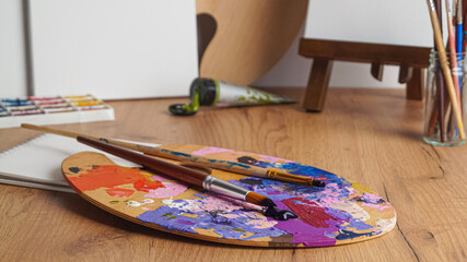 Artist's palette with mixed paints and brushes on wooden table