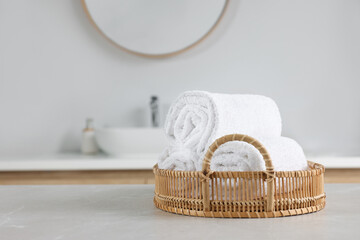 Wicker basket with white towels on table in bathroom. Space for text