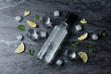 Obraz na płótnie Canvas Bottle of vodka, shot glasses, lemon, mint and ice on black marble table, flat lay