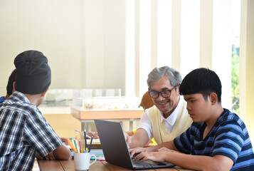 Asian boys are sitting infront of asian elderly teacher inside the room to ask and to do the school project work and listening to the elderly teacher about their project work, soft and selective focus