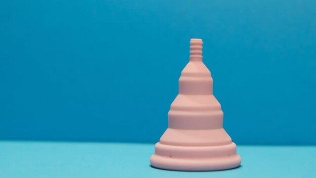 4k v&iacute;deo movimiento de copa menstrual rosa plegable en fondo azul vista de frente con copy space