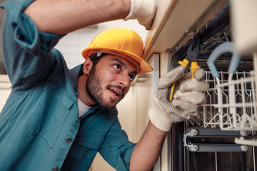 Service man repairing dishwasher in modern kitchen. Maintenance and household assistance concept 