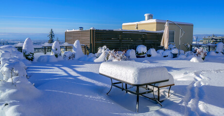 Thick snow covering deck furniture, plants and shrubs on a BC rooftop patio in winter.