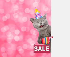 Happy cat wearing a birthday cap shows signboard with labeled "sale" and looks from  behind empty white banne.  Shade trendy color of the year 2023 - Viva Magenta background. Empty space for text