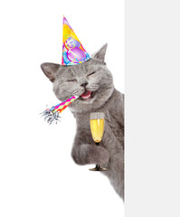 Happy cat wearing party cap holds party horn and glass of champagne looks from behind empty white banner. isolated on white background