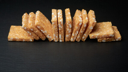 coconut biscuits, textured crispy square shaped homemade cookies isolated on black table surface, selective focus with copy space