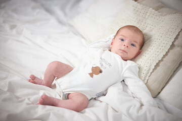 A charming boy in a white sunny bedroom. A newborn baby is resting in bed. Nursery for small children. Textiles and bed linen for children. Family morning at home.