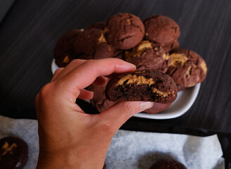 Woman's hand showing a fluffy thick chocolate brownie cookie cut in half with peanut 