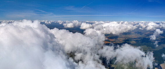 Aerial view from airplane window at high altitude of earth covered with puffy cumulus clouds forming before rainstorm