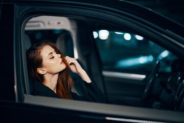 Obraz na płótnie Canvas a stylish, luxurious woman is sitting in a black car at night, straightening her long, styled hair, closing her eyes with pleasure